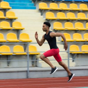 Photo of young african athlete man run on running track outdoors. Looking aside.